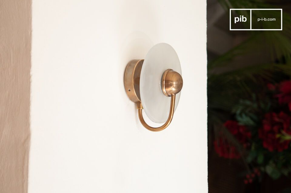 The Graham wall light is designed with a round gilded brass base and a curved arm that ends in a